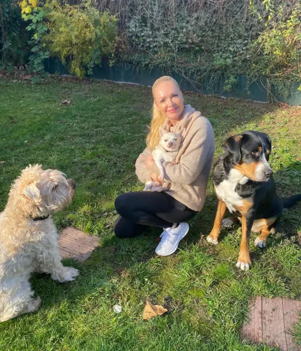 Katrin Pantos sitzt mit drei Hunden auf einer Wiese.